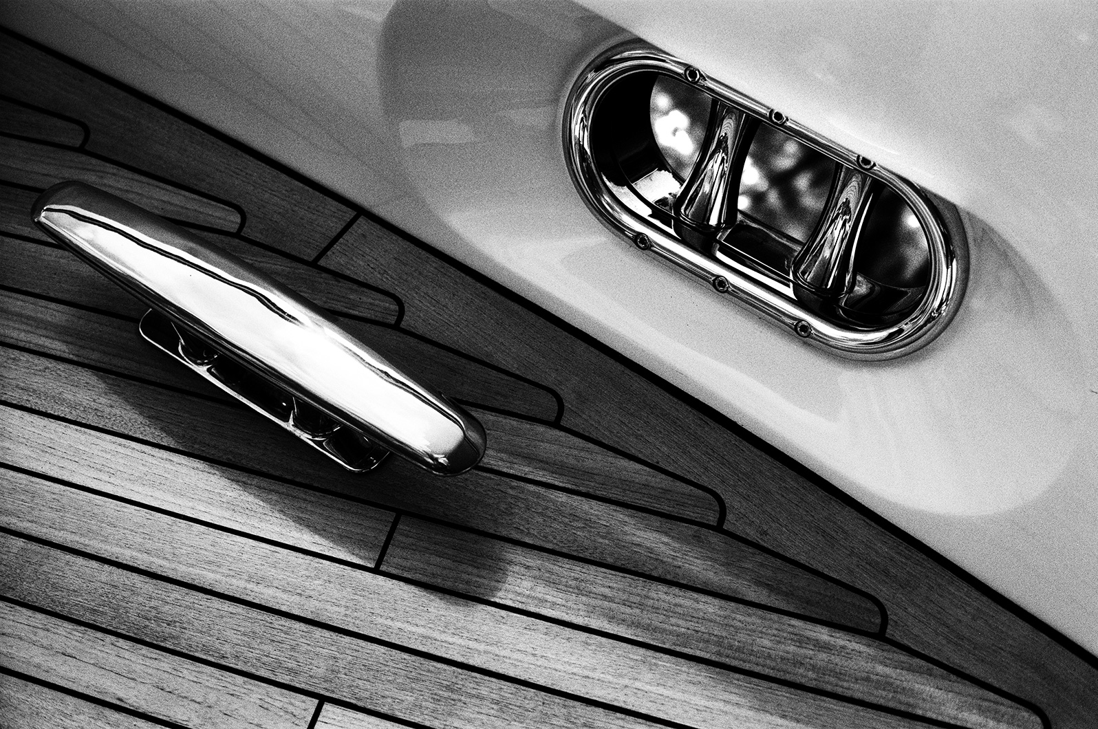 Black and white close-up of a yacht deck cleat and fairlead set into wooden decking.