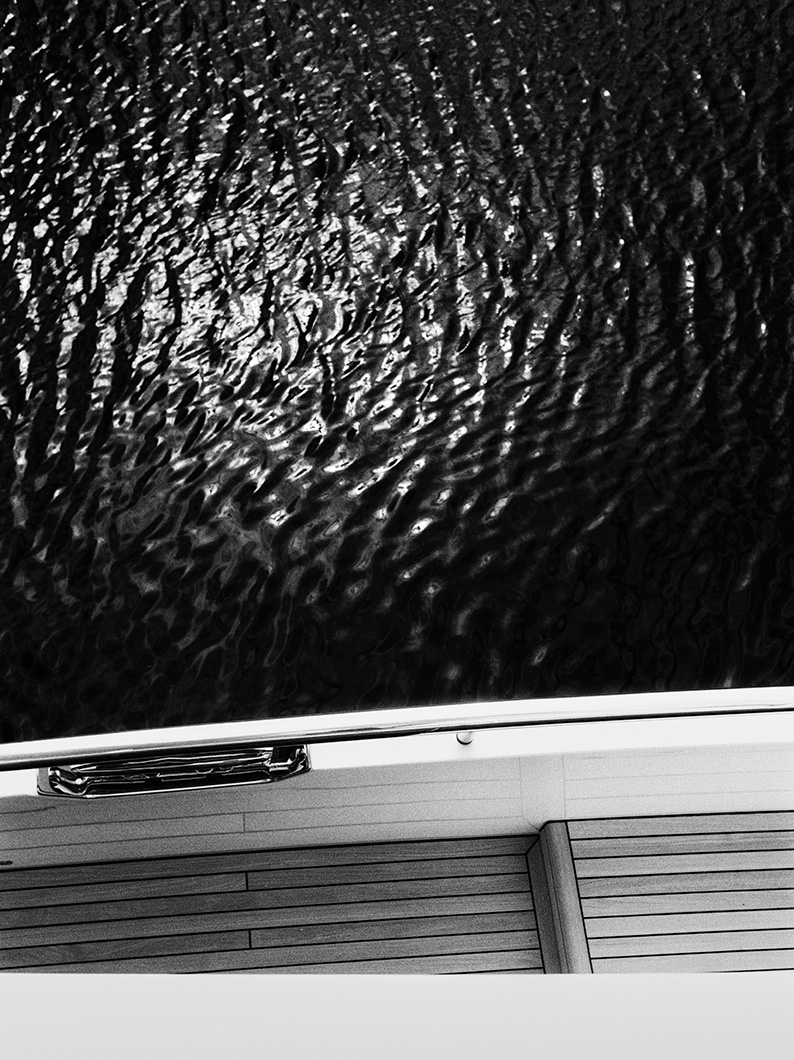 Black and white view from a yacht looking down at rippling water beside the deck.