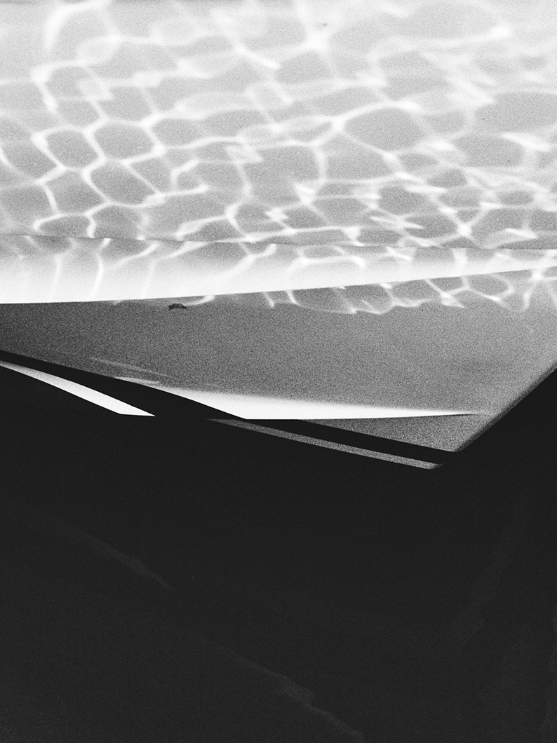 Black and white close-up of a yacht hull with rippling water reflections across its surface.