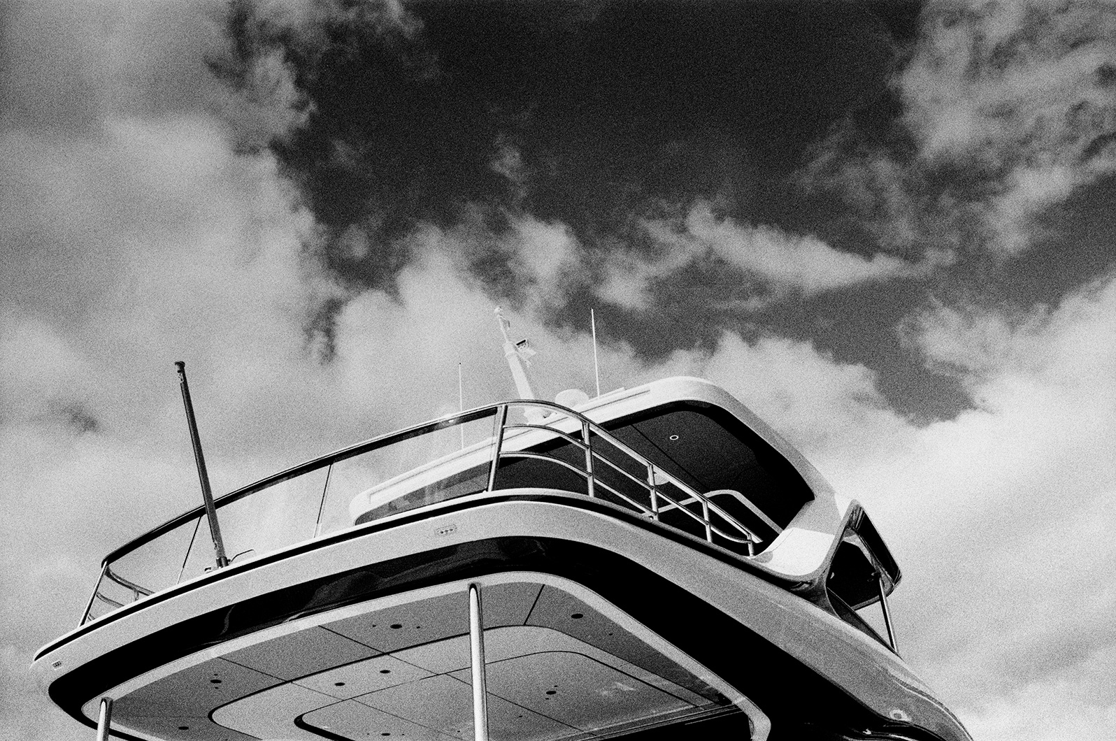 Black and white photo of a yacht upper deck viewed from below, with railings, overhang, and cloudy sky background.