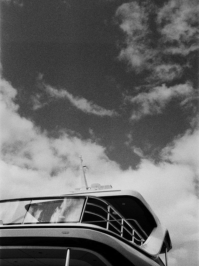 Black and white image of a yacht’s bridge and upper deck against a cloudy sky.