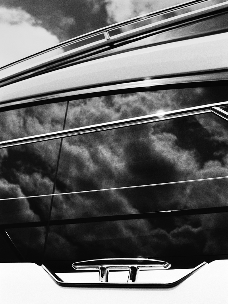 Reflection of dramatic clouds on the tinted glass and polished chrome rails of a yacht in black and white.