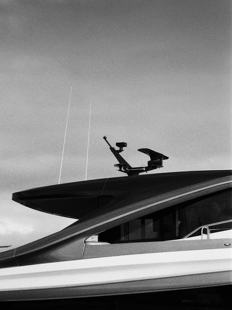 Black and white close-up of a yacht flybridge roof and radar mast, with antennas rising against the sky.