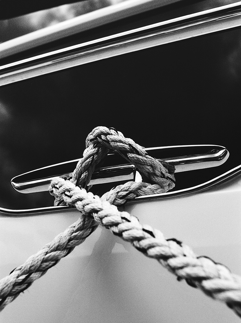 Black and white close-up of braided mooring rope tied around a polished metal cleat on a yacht.