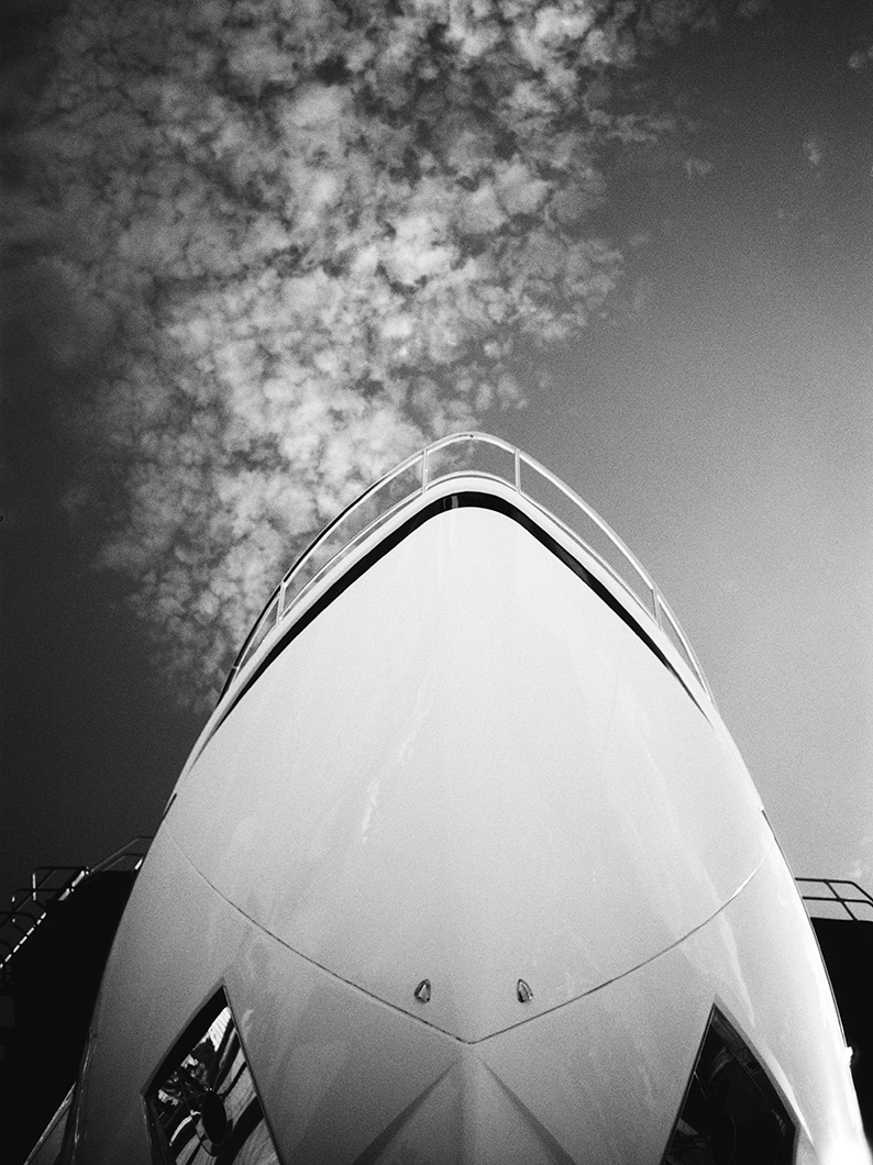 Black and white photo looking up at the bow of a yacht against a cloudy sky.