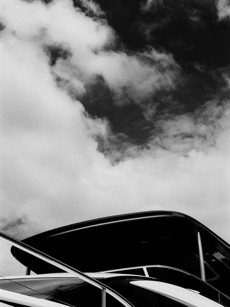 Black and white photo showing the roofline and railings of a yacht with clouds filling the sky above.