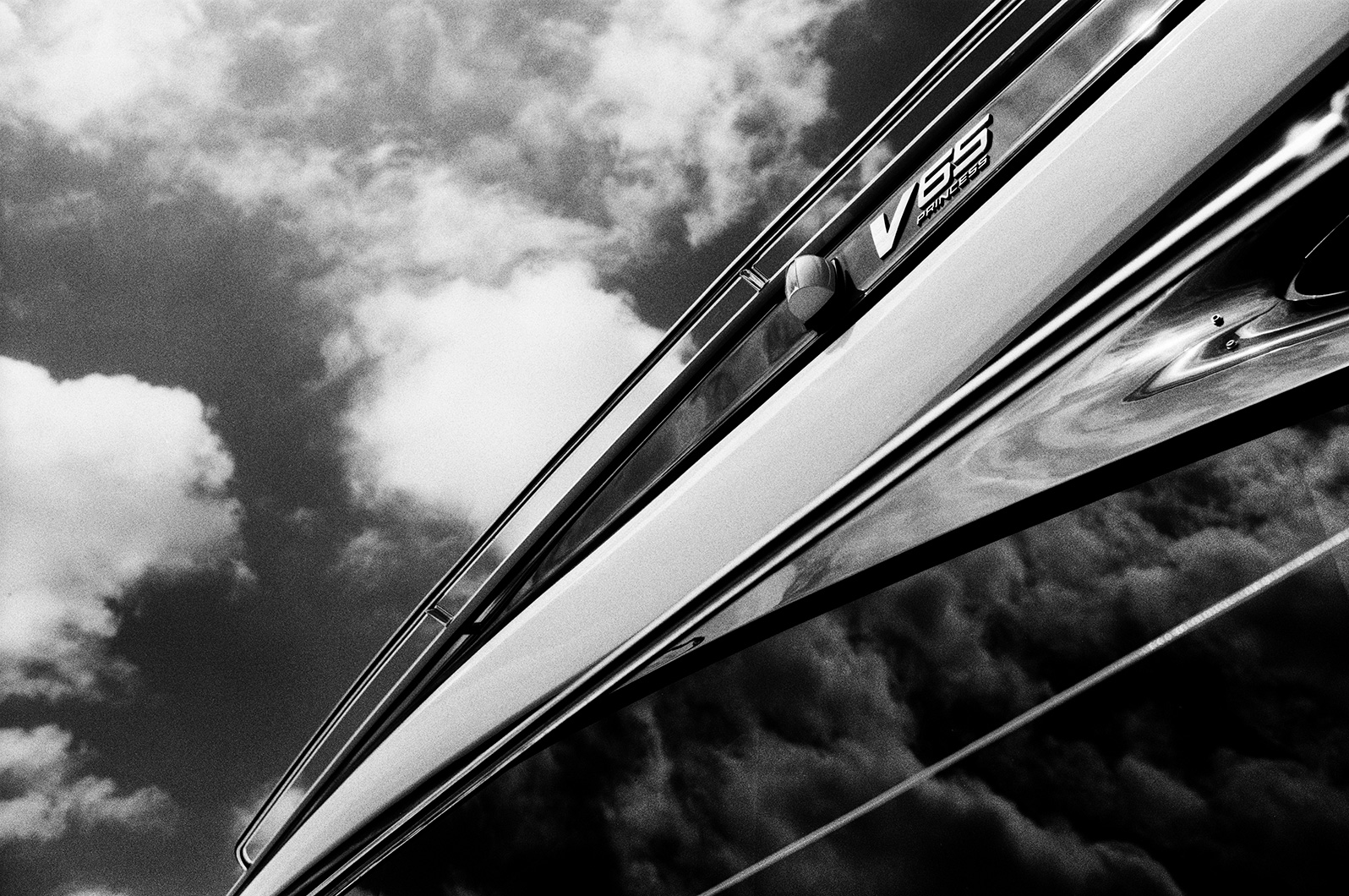 Black and white angled photo of a Princess V65 yacht’s side, with reflections of clouds in the windows.
