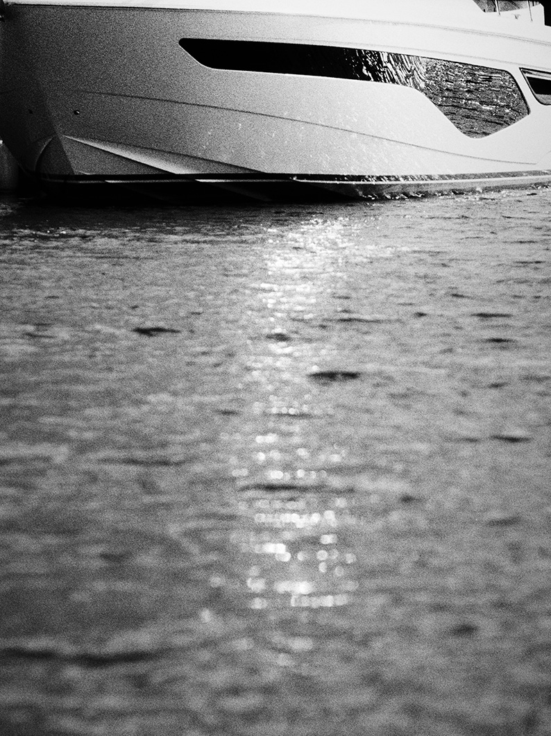 Black and white photo of a Princess yacht bow at water level, with sunlight reflecting across the rippling surface.
