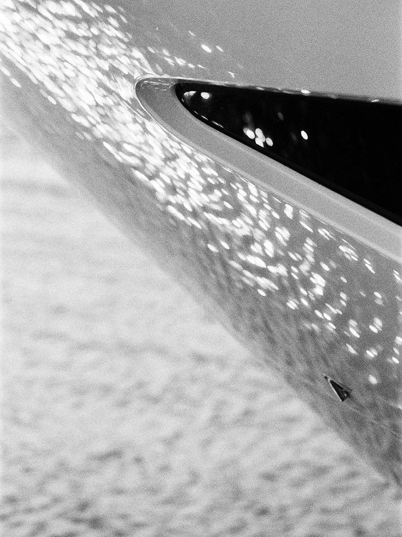 Black and white close-up of a Princess yacht hull detail, showing water reflections sparkling across its surface.