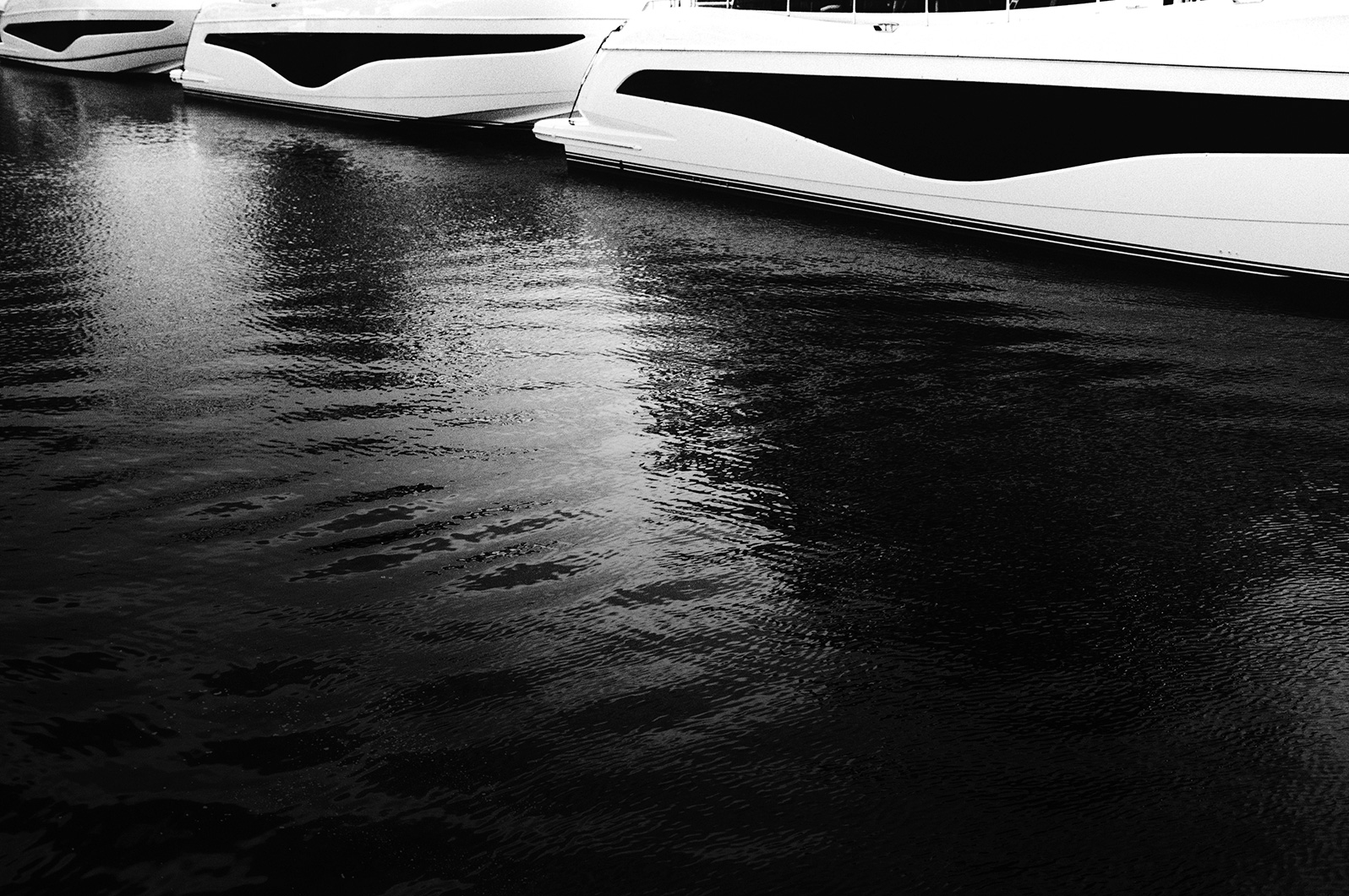 Black and white photo of multiple Princess yachts moored side by side, with their hulls reflected in the water.