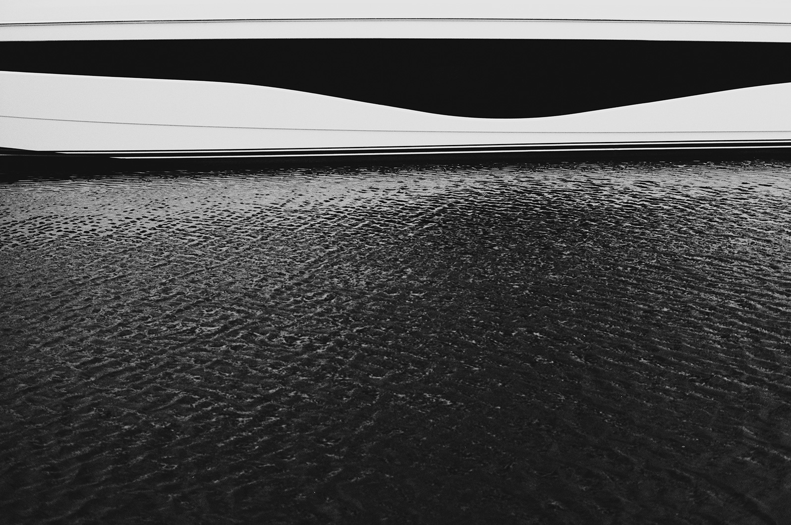 Black and white photo showing the side hull of a Princess yacht above rippling water.