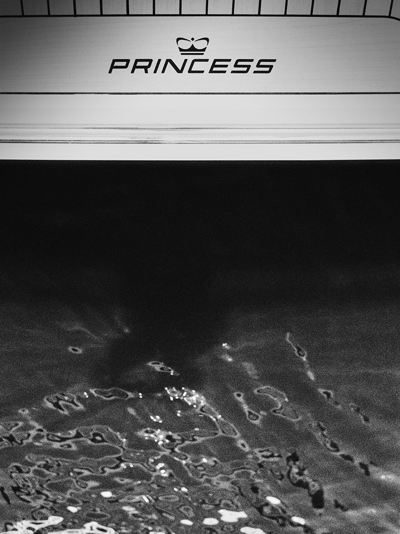 Black and white close-up of the Princess logo on a yacht’s stern above the waterline.